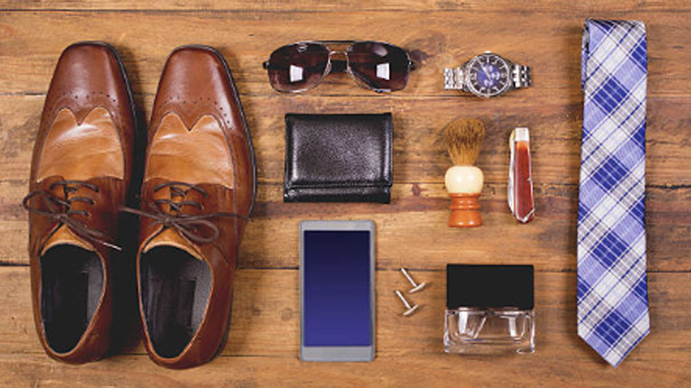 Men's accessories organized on table in knolling arrangement Variety of men's accessories organized in knolling arrangement.  Items include: dress shoes, tie, sunglasses, wallet, watch, shaving brush, cologne, and smart phone.  The items all lie on a wooden desk or table.   Men's personal accessories, clothing themes.  Father's Day.  Fashion.  Business.  Retail.